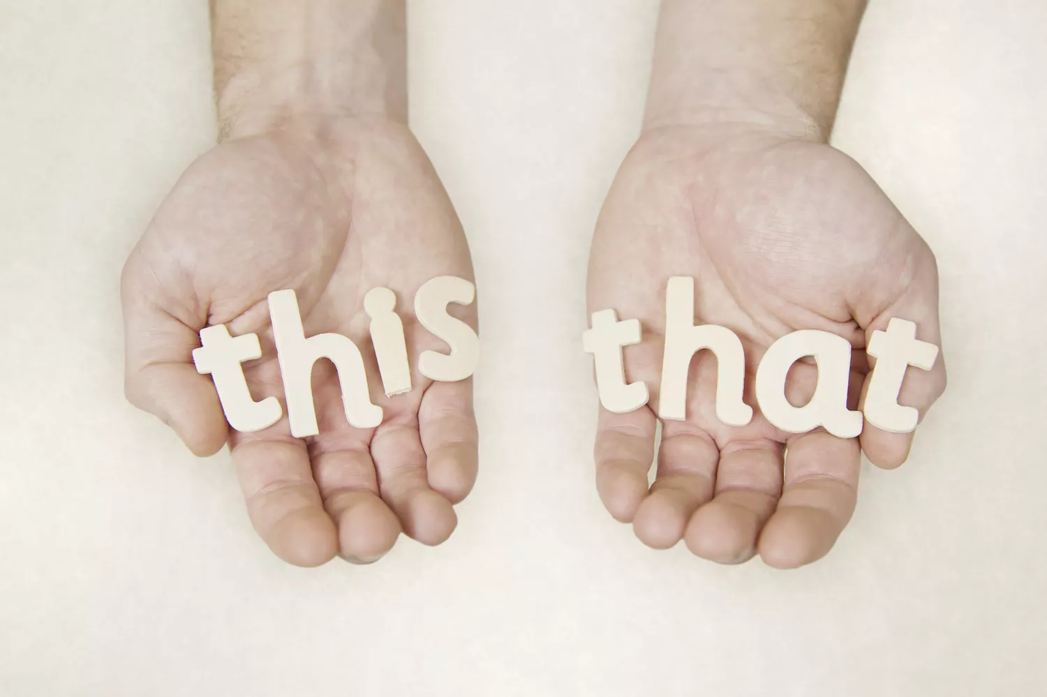 Hands holding block letters that read "this" and "that"