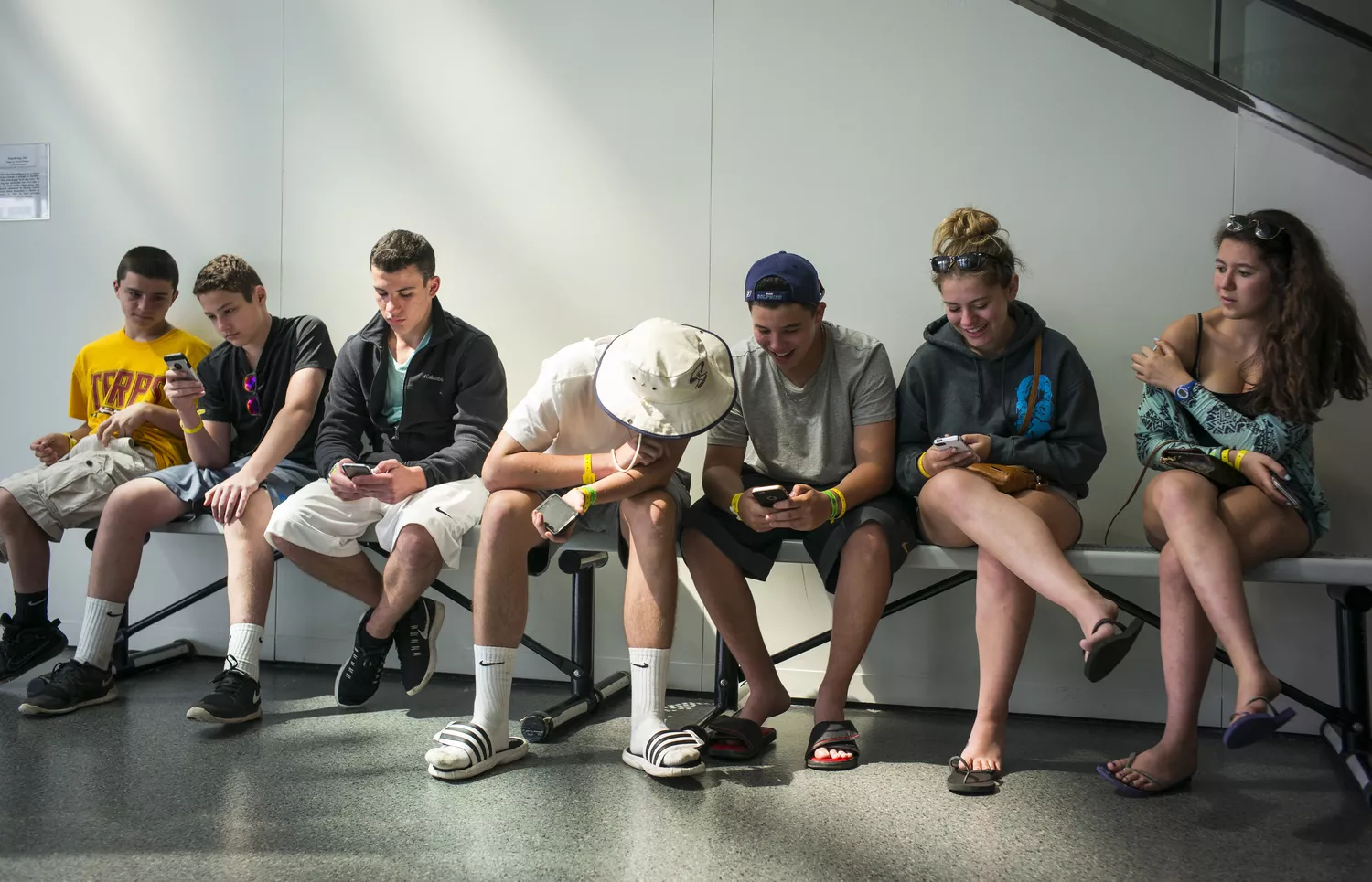 teens sitting on bench using smartphones
