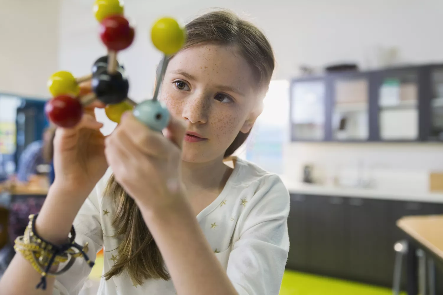 Young girl studying a model of a molecule.