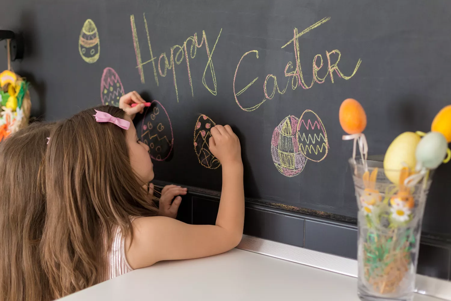 Two cute girls drawing easter eggs on blackboard