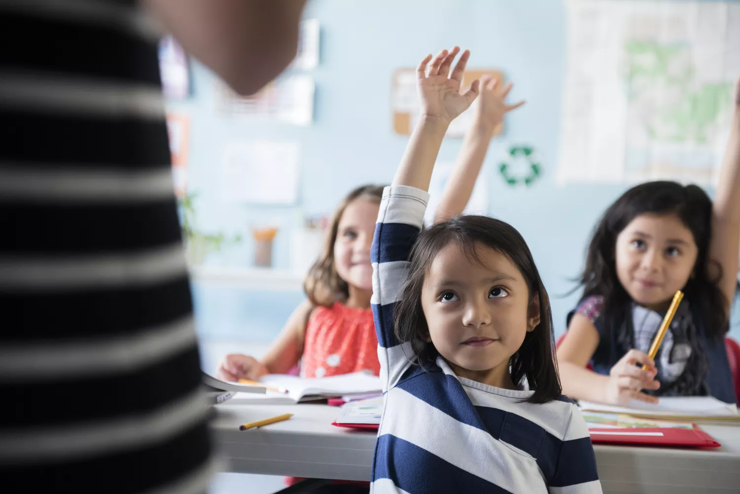 Cute children in a classroom with their hands raised